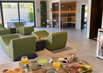 Ontbijtarrangement op tafel in de privéwellness van Total Care, met ligzetels en sauna op de achtergrond